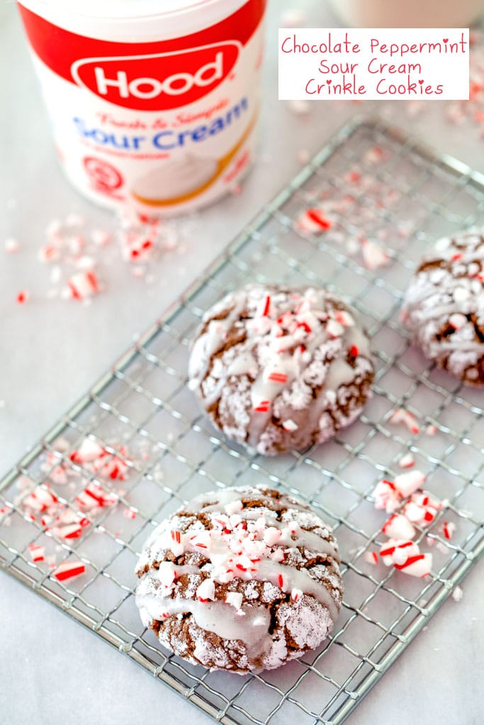 Overhead view of chocolate peppermint sour cream crinkle cookies on a cooling rack with crushed candy canes and a container of sour cream in the background with recipe title at top