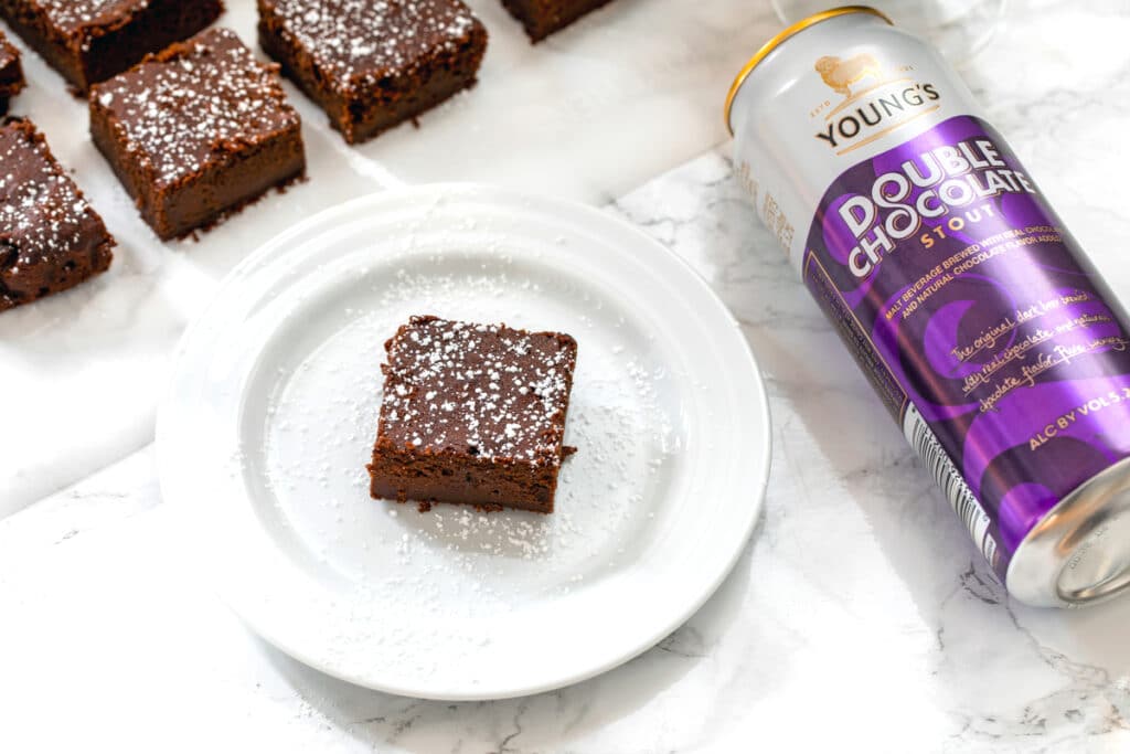 Landscape overhead photo of chocolate stout brownie with can of Young's Double Chocolate Stout and more brownies lined up in background