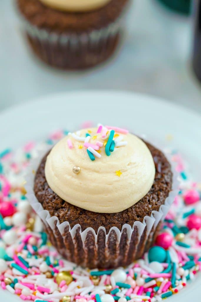 Overhead view of chocolate stout cupcake with Baileys frosting and sprinkles on a white plate covered in sprinkles