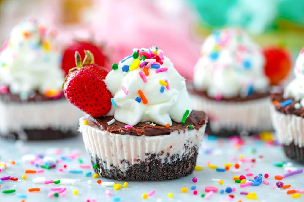 Landscape head-on view of chocolate strawberry ice cream cupcake surrounded by more cupcakes and sprinkles in background