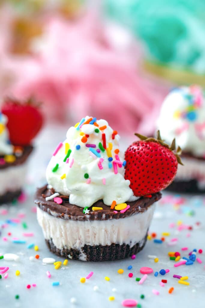 Head-on view of a chocolate strawberry ice cream cupcake with sprinkles all around and more cupcakes in background
