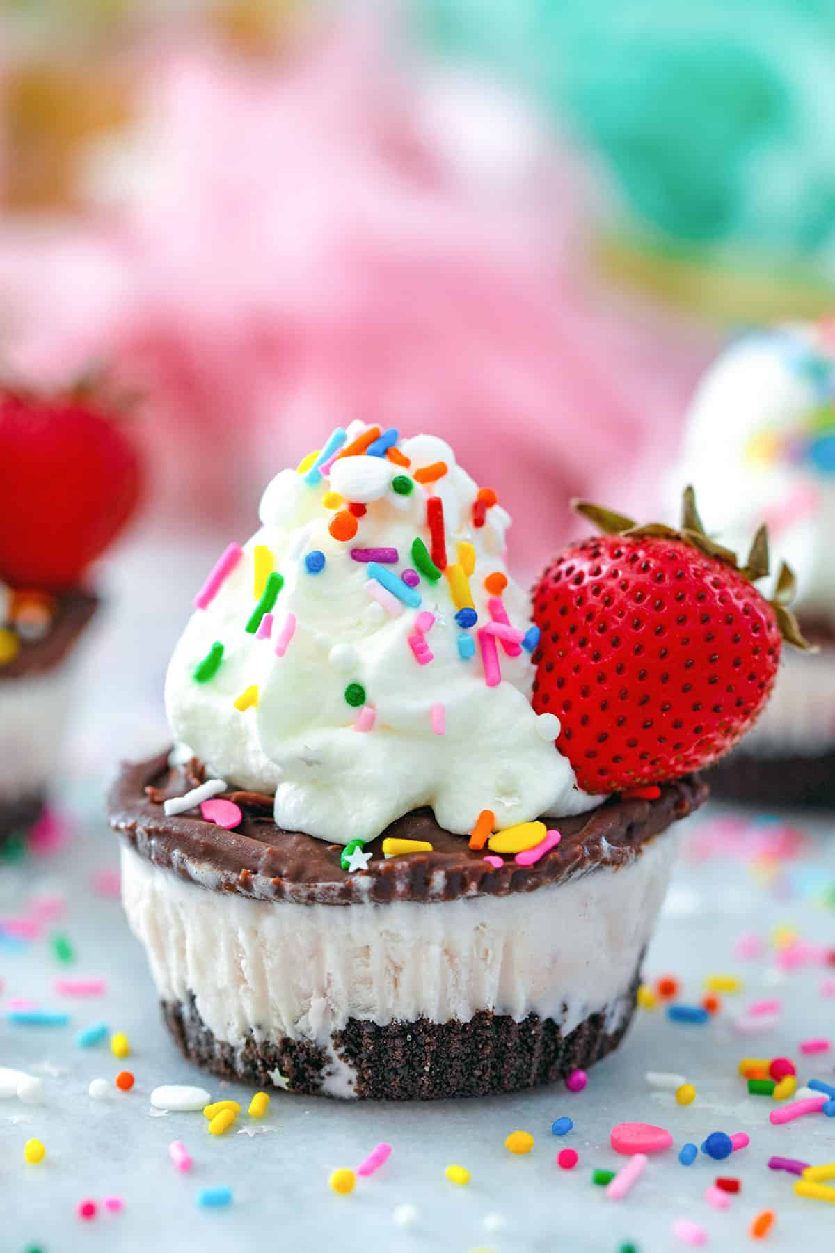 Head-on closeup view of a chocolate strawberry ice cream cupcake with sprinkles all around.
