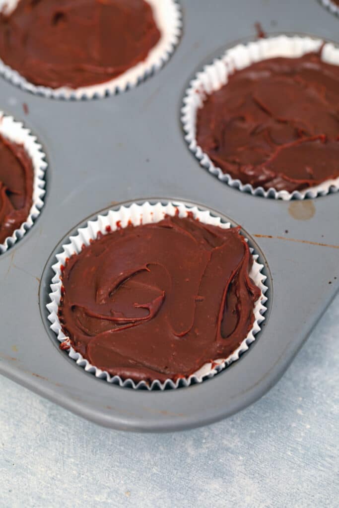 Chocolate fudge sauce smoothed over ice cream in cupcake papers in tin