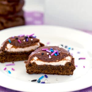 A chocolate surprise cookie cut in half showing marshmallow filling with sprinkles all around