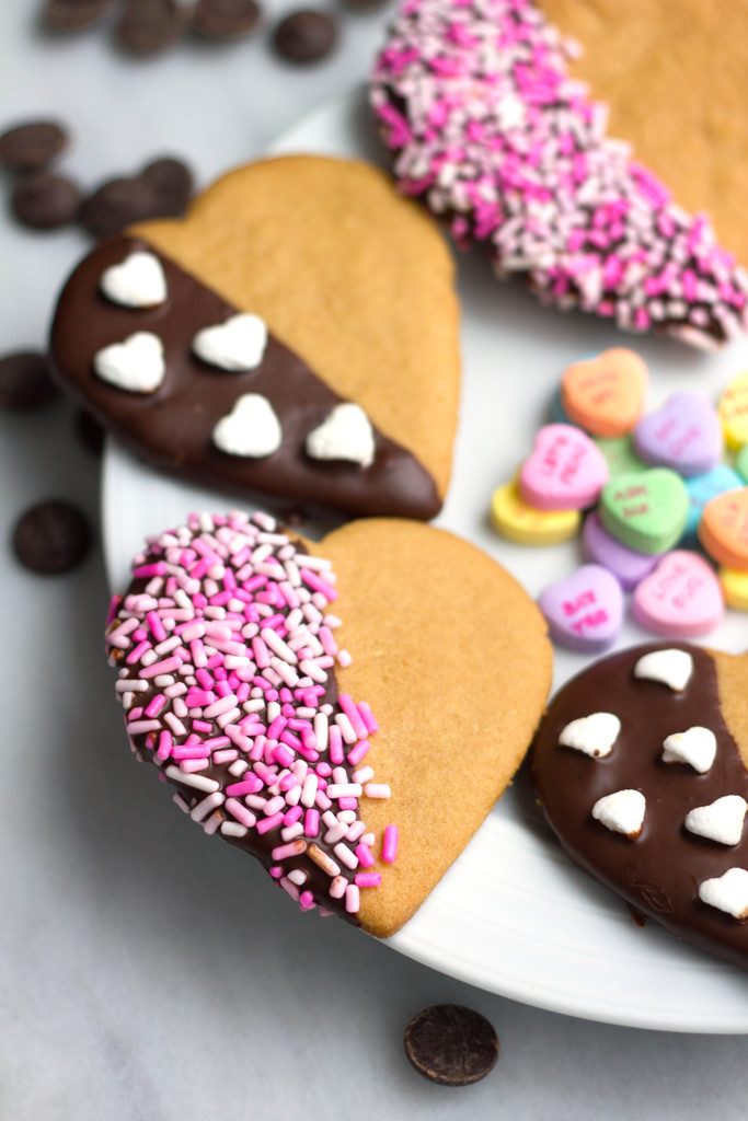 Overhead view of a plate full of chocolate-dipped peanut butter heart cookies with sprinkles and mini heart marshmallows with conversation hearts in the center of the plate