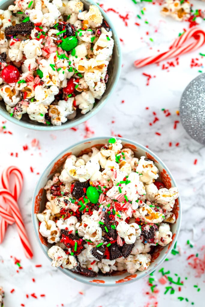 Overhead view of two bowls of Christmas popcorn with candy canes, sprinkles, and ornaments around