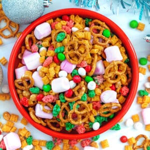 Overhead closeup view of a bowl of Christmas trail mix with trail mix and ornaments on the table