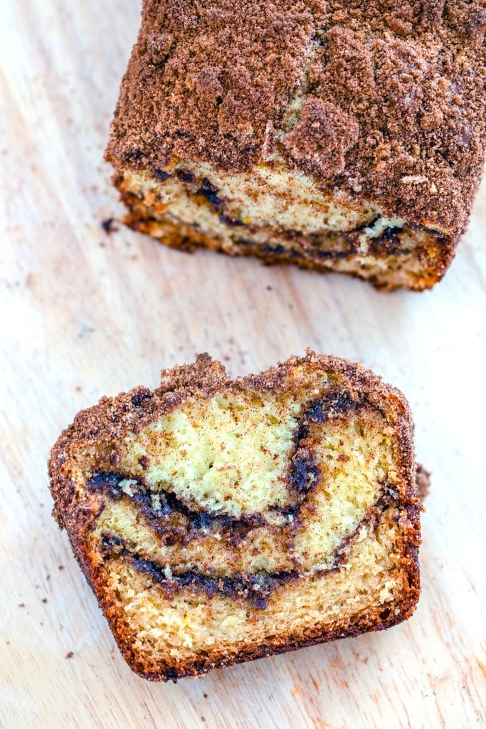 Overhead view of a slice of cinnamon loaf cake on a wooden cutting board with the rest of the loaf in the background