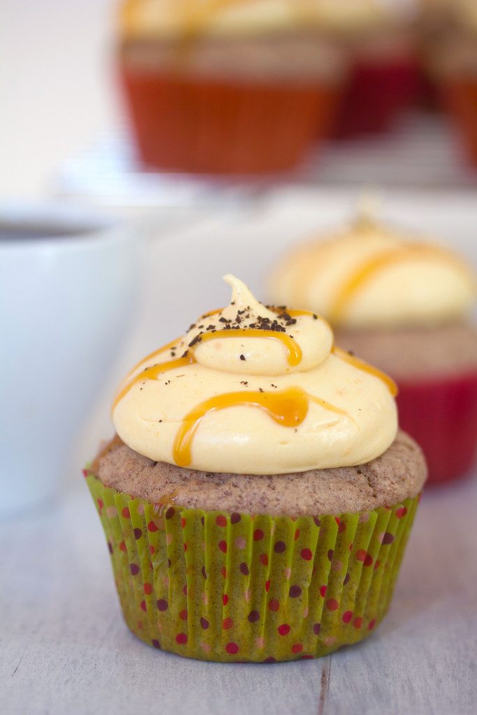 Head-on close-up view of a cinnamon cupcake with pumpkin coffee cream cheese frosting and a caramel drizzle