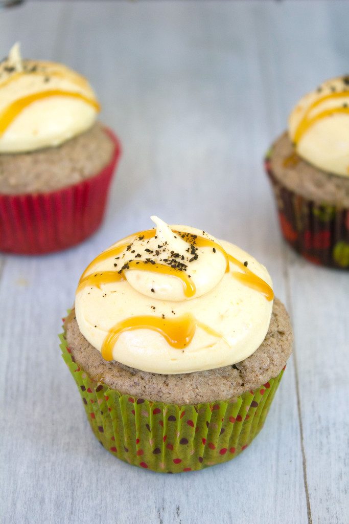 Overhead view of a cinnamon cupcake with pumpkin coffee cream cheese frosting with caramel drizzle with more cupcakes in the background