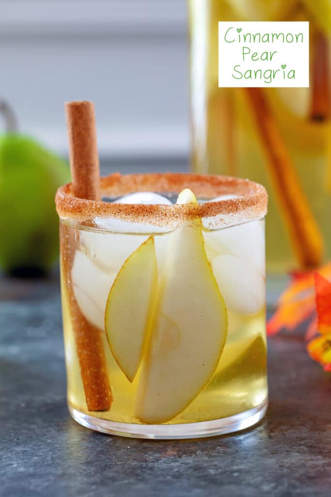 Head-on closeup view of a cinnamon sugar rimmed glass of cinnamon pear sangria with cinnamon stick garnish and recipe title at top
