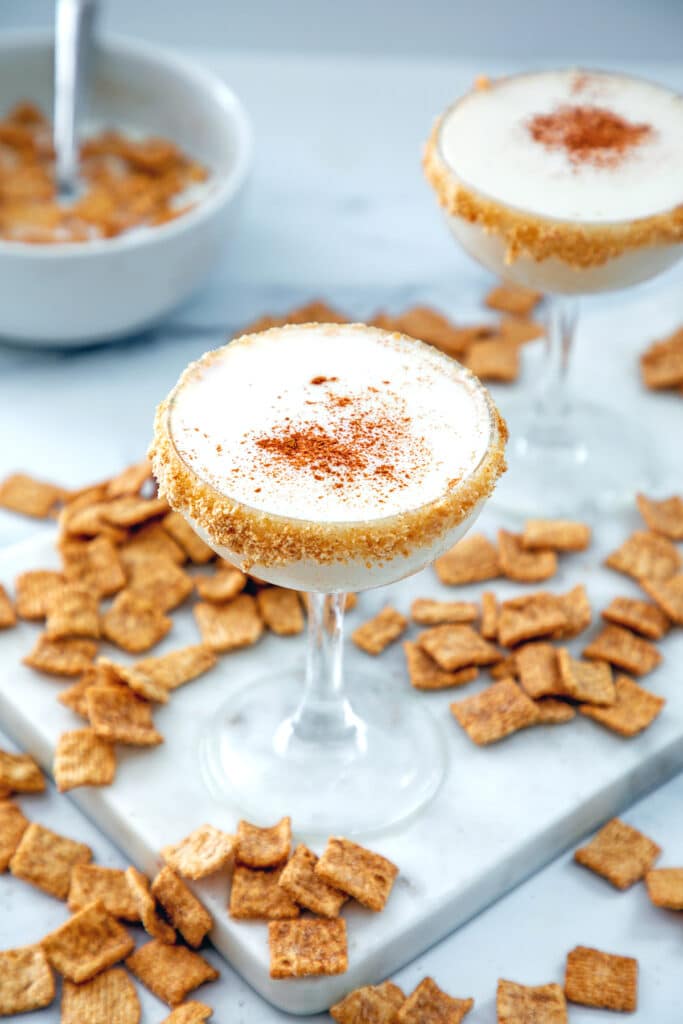 Overhead view of two Cinnamon Toast Crunch cocktails with cereal all around and bowl of cereal in background