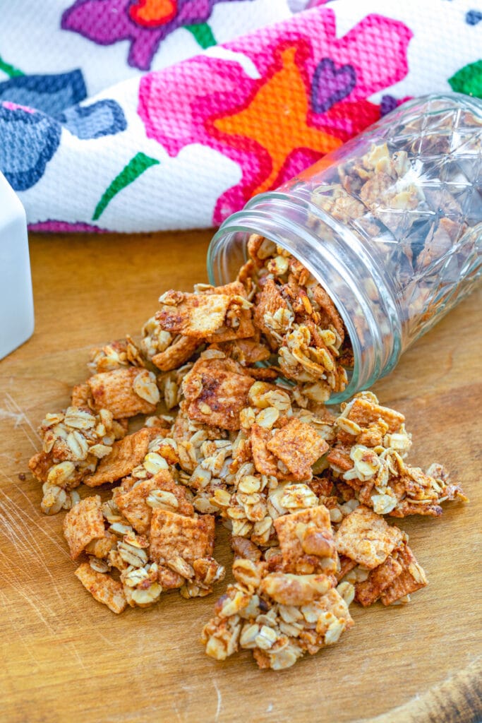 Overhead closeup view of Cinnamon Toast Crunch granola spilling out of a jar on a wooden board