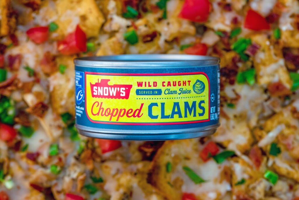 Can of chopped clams sitting over a platter of clam nachos