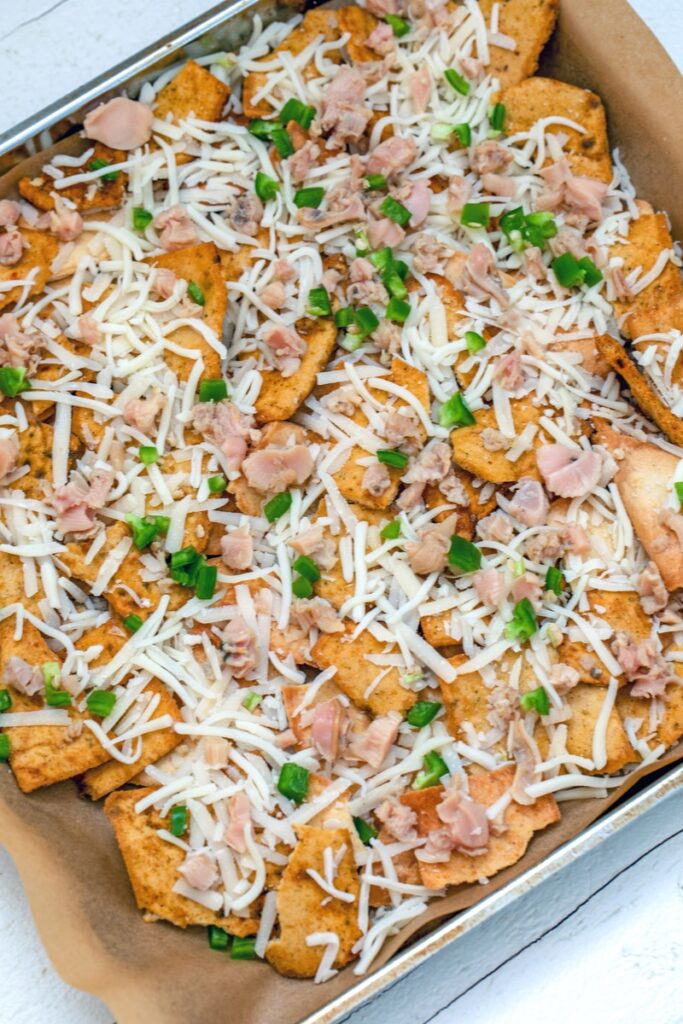 overhead view of clam nachos in the process of being made with pita chips, jalapeño, shredded cheese, and chopped clams