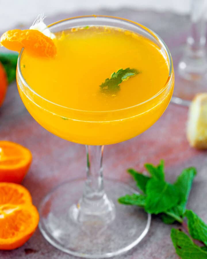 Clementine ginger cocktail in a coupe glass with clementines, ginger, and mint all around