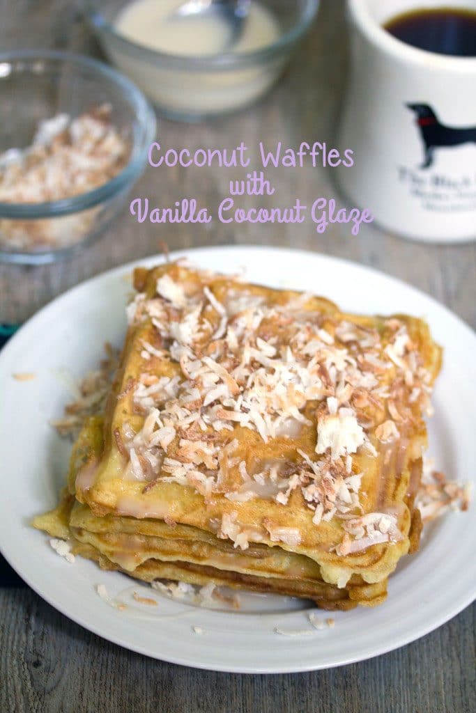 Overhead view of coconut waffles with vanilla coconut glaze topped with toasted coconut with coffee cup and bowls of toasted coconut and glaze in the background and "Coconut Waffles with Vanilla Coconut Glaze" text on top