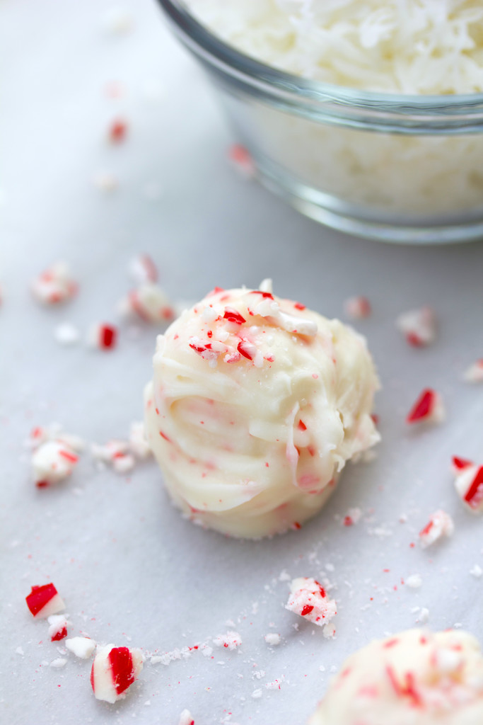 Coconut candy cane truffles on white surface with crushed candy canes all around and bowl of shredded coconut in the background