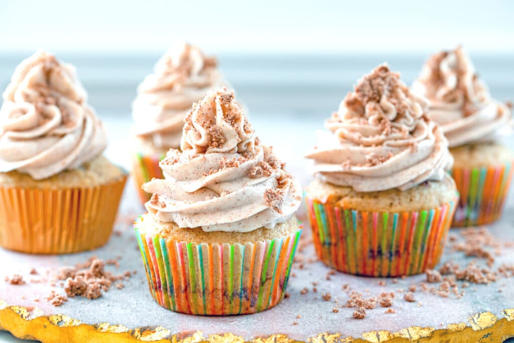 Head-on landscape view of multiple coffee cake cupcakes on a pink and gold marble tray surrounded by crumb topping