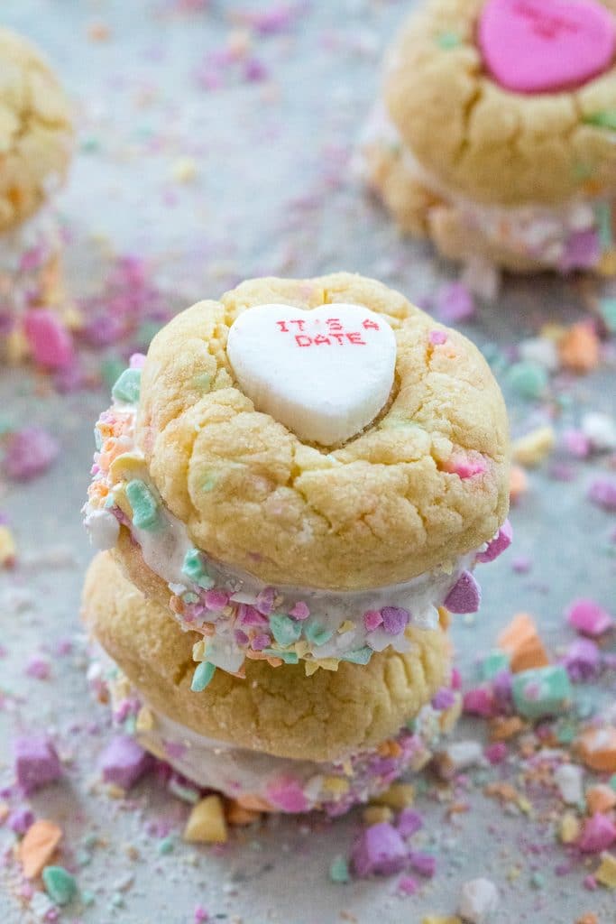Head-on view of two conversation heart sandwich cookies with marshmallow fluff stacked on each other and surrounded by lots of crushed conversation hearts