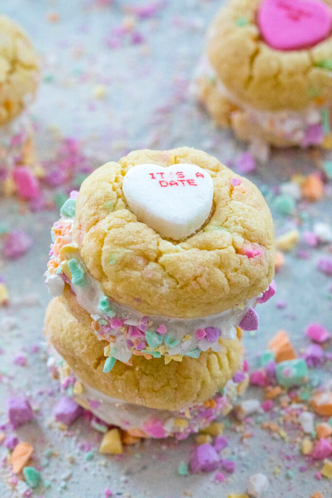 Head-on view of two conversation heart sandwich cookies with marshmallow fluff stacked on each other and surrounded by lots of crushed conversation hearts.