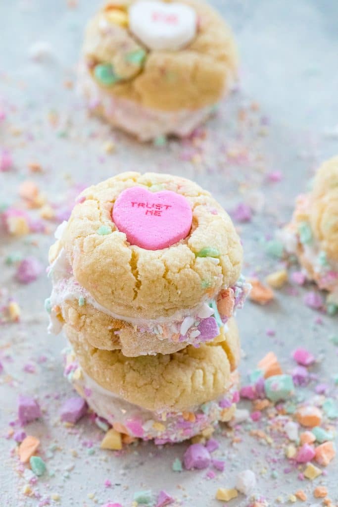 Head-on view of a stack of two conversation heart sandwich cookies with marshmallow fluff with more conversation heart cookies in background and crushed conversation hearts all around.