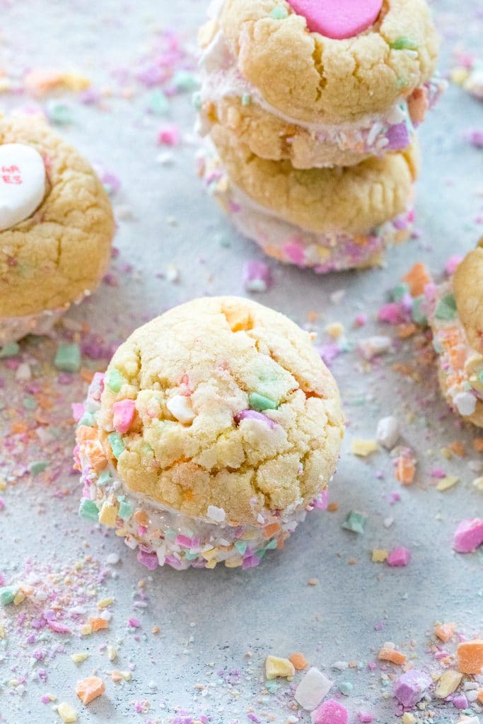 Overhead view of conversation heart sandwich cookies, some with large conversation heart in the center and some without, with crushed conversation hearts all around