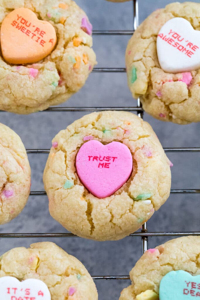 Overhead view of conversation heart cookies topped with large conversation hearts on a baking rack.