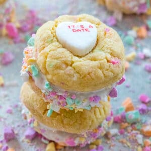 Two conversation heart sandwich cookies with fluff stacked on each other with crushed conversation hearts all around