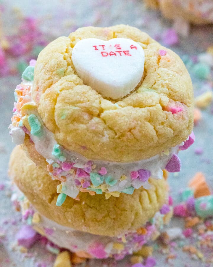 Two conversation heart sandwich cookies with fluff stacked on each other with crushed conversation hearts all around