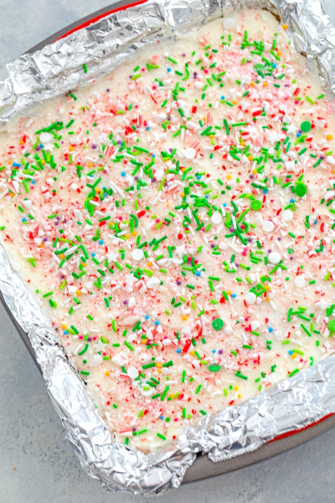 Overhead view of candy cane cookie dough bars with crushed candy cane and green sprinkle topping in baking pan