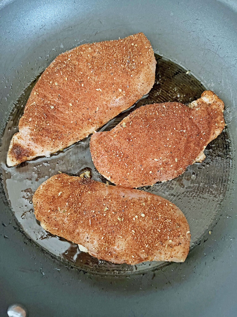 Chicken breasts with spices cooking in skillet.