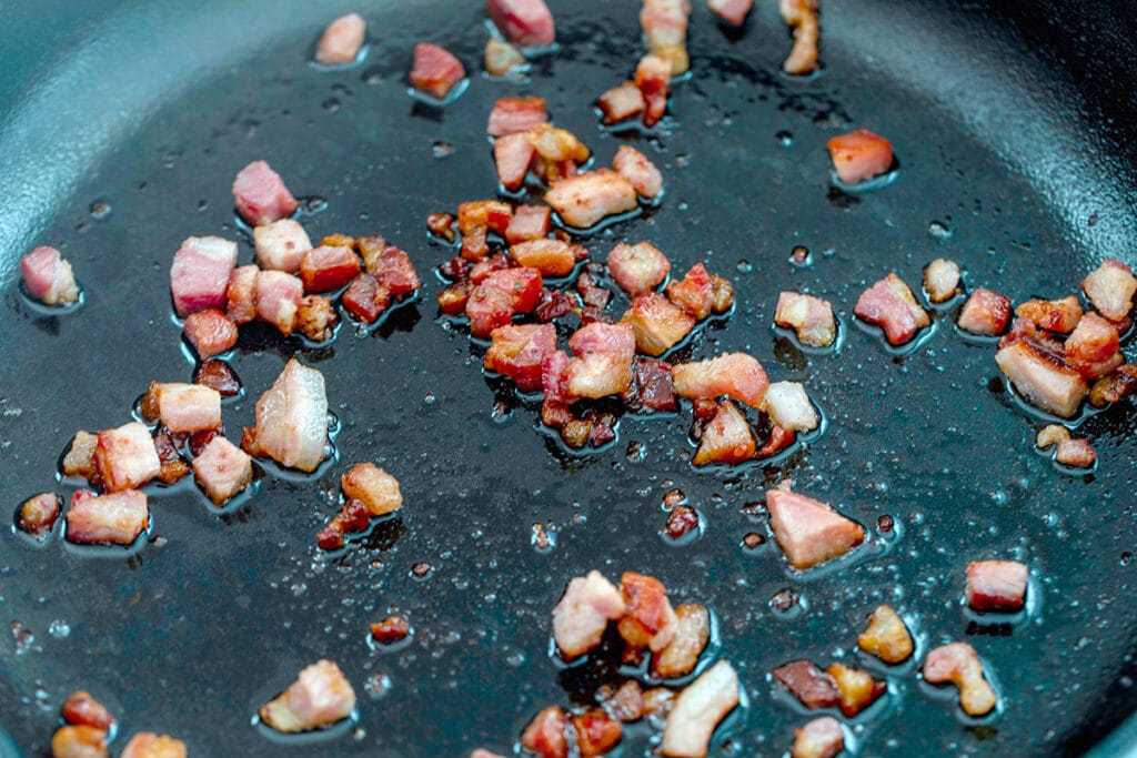 Overhead landscape view of diced pancetta cooking in a skillet