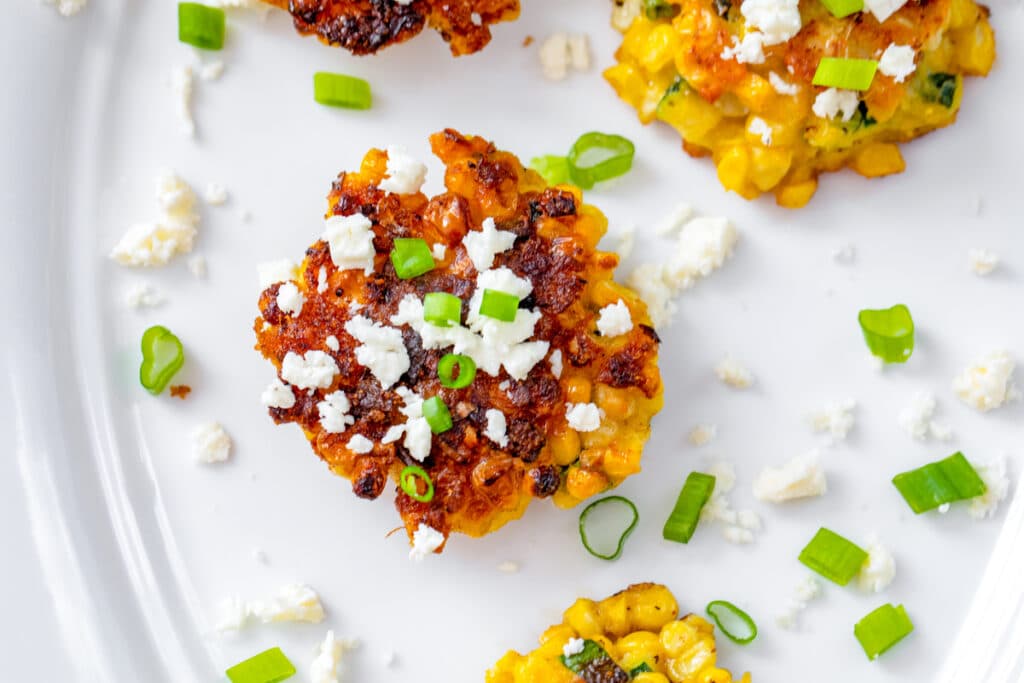 Landscape overhead view of a fresh corn cake on a white platter topped with crumbled feta and scallions