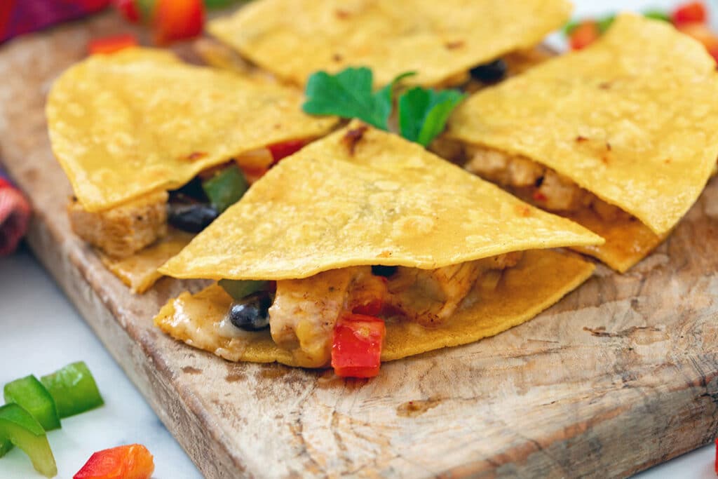 Landscape head-on view of a corn tortilla quesadilla with cheese, chicken, and pepper filling oozing out.