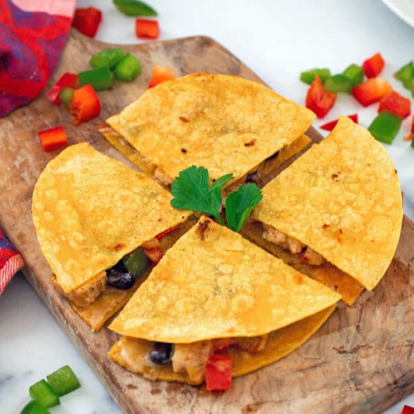 Overhead closeup view of a corn tortilla quesadilla cut into four wedges with peppers all around.