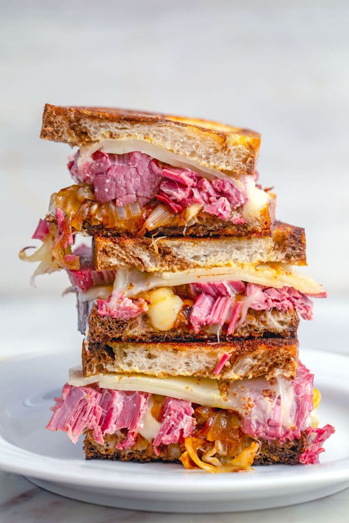 Head-on view of corned beef melts stacked on a white plate.