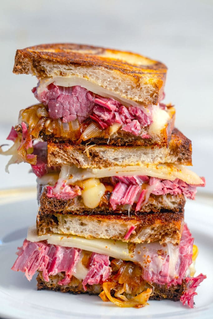 Head-on view of three halves of corned beef melts sandwiches stacked on top of each other on a white plate.