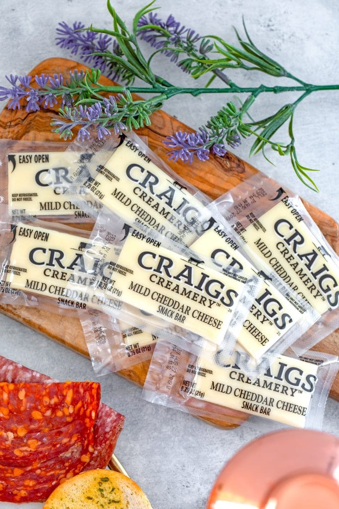 Overhead view of multiple Craigs Creamery cheese snack bars on a wooden board with flowers in the background