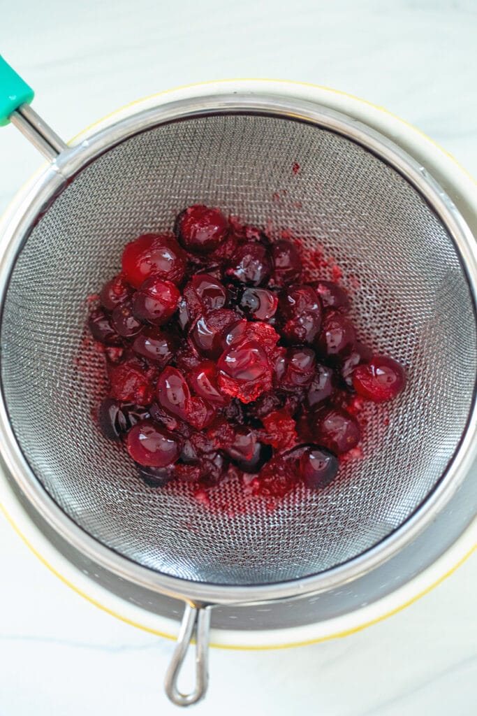 Cranberries being strained out of syrup into bowl
