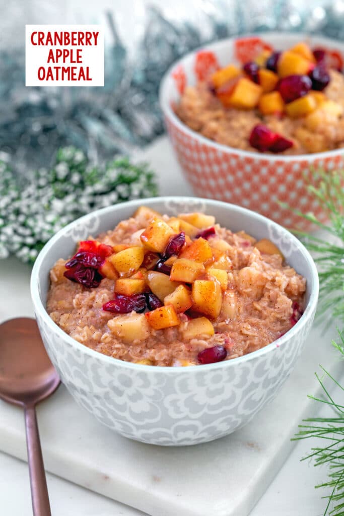 Head-on view of a bowl of cranberry apple oatmeal with second bowl and holiday garland in background and recipe title at top