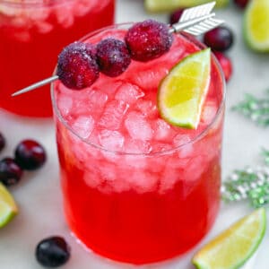 Overhead view of a cranberry gin cocktail with second drink in background and cranberries and lime wedge garnish