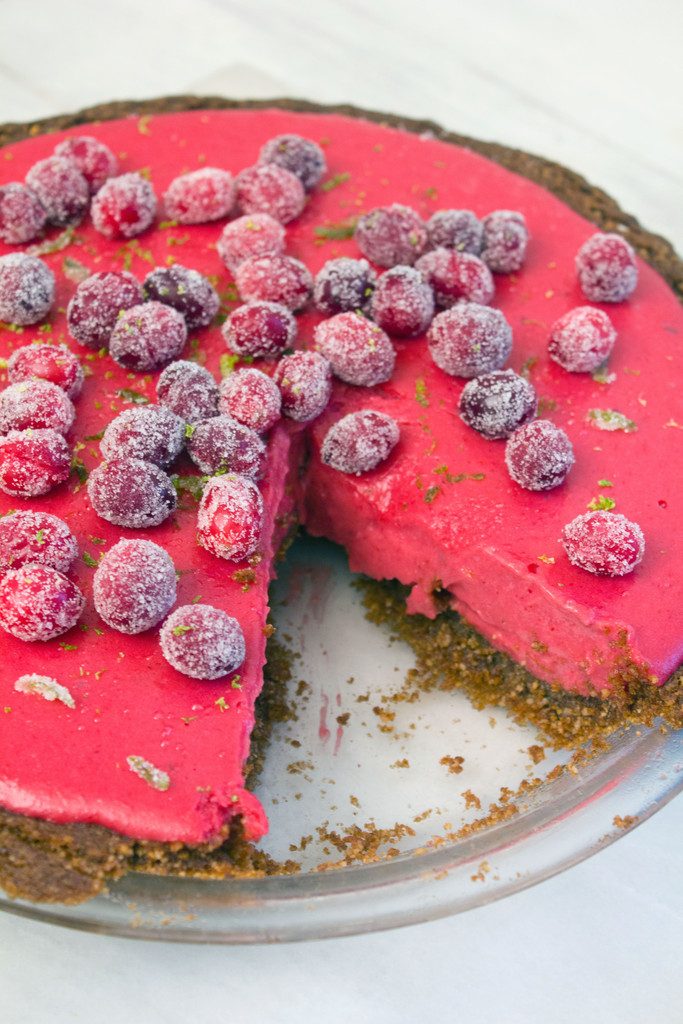 Overhead view of cranberry lime pie in a pie plate topped with sugared cranberries and lime zest with a slice removed