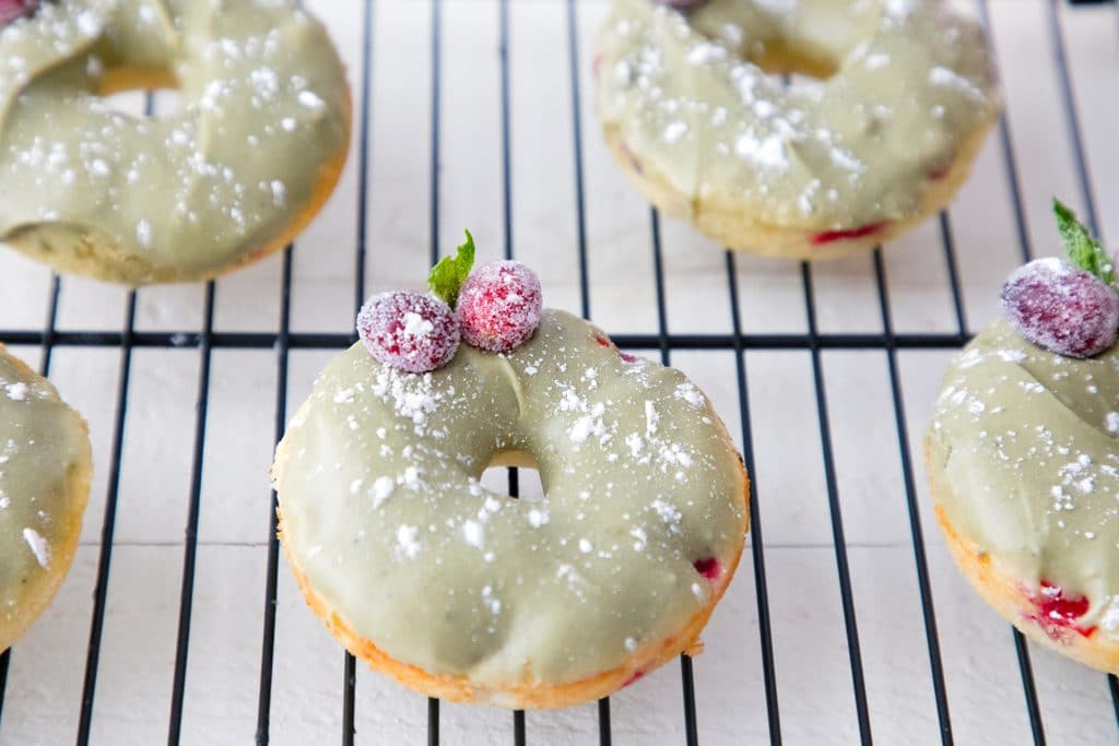 Landscape view of multiple cranberry matcha donuts on baking rack