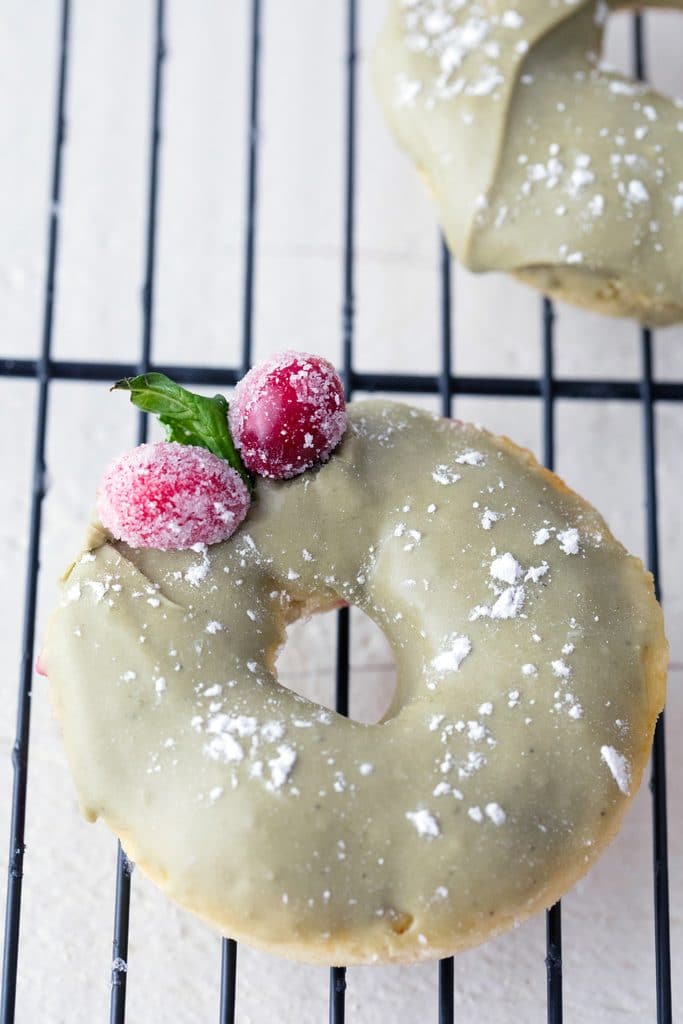 Overhead close-up view of a cranberry matcha donut with sugared cranberry garnish on baking rack