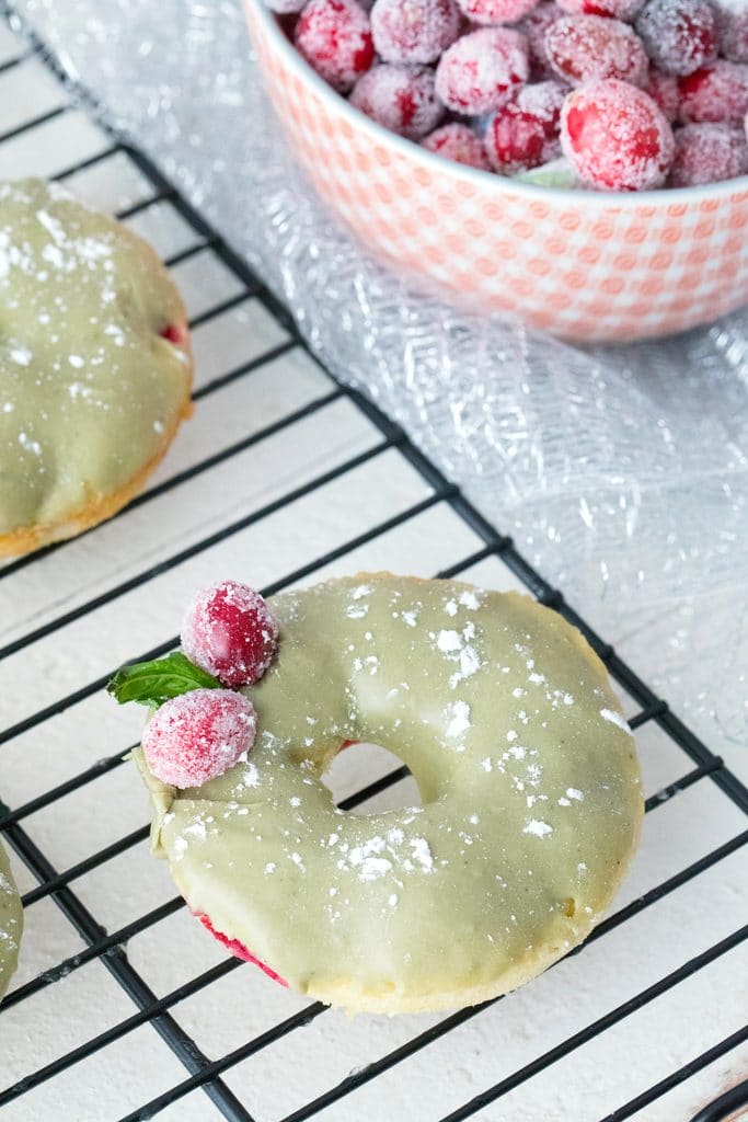 Overhead view of cranberry matcha donut on a baking rack with bowl of sugared cranberries in background