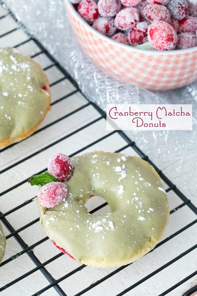 Overhead view of cranberry matcha donut on a baking rack with bowl of sugared cranberries in background and recipe title text on image