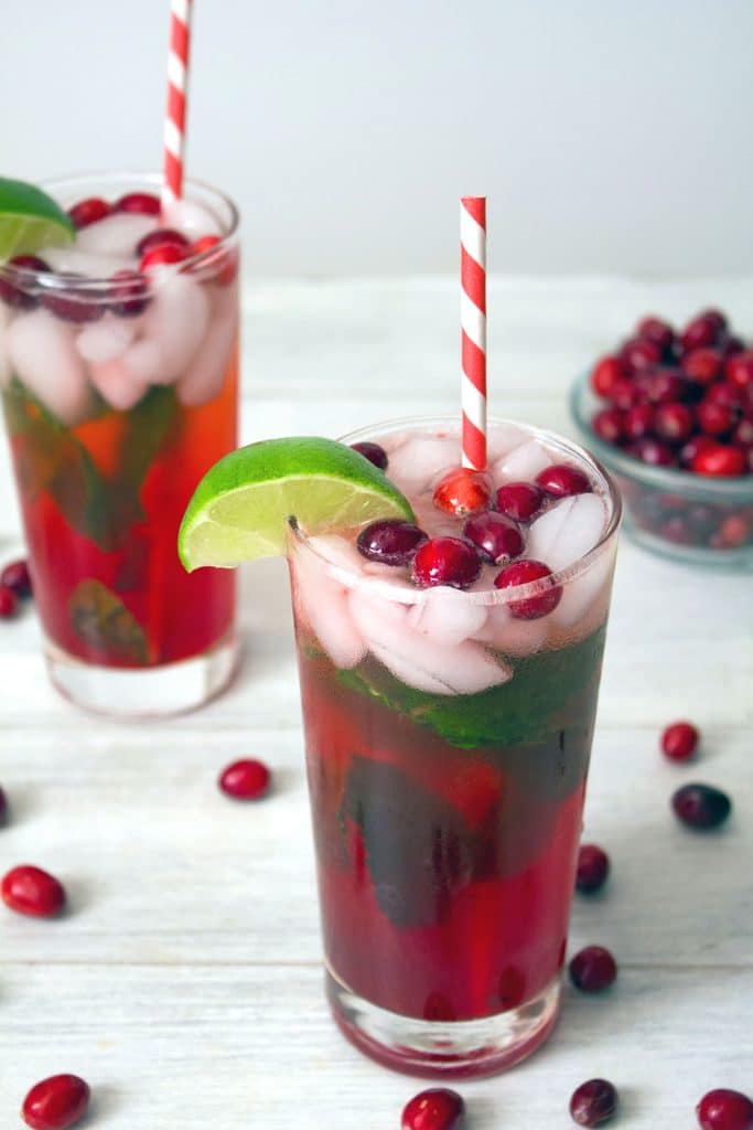 Overhead view of two cranberry mojitos garnished with a lime wedge and cranberries with red and white striped straws and cranberries scattered around
