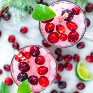 Overhead view of two cranberry mojitos with red and white straws, limes, and cranberries