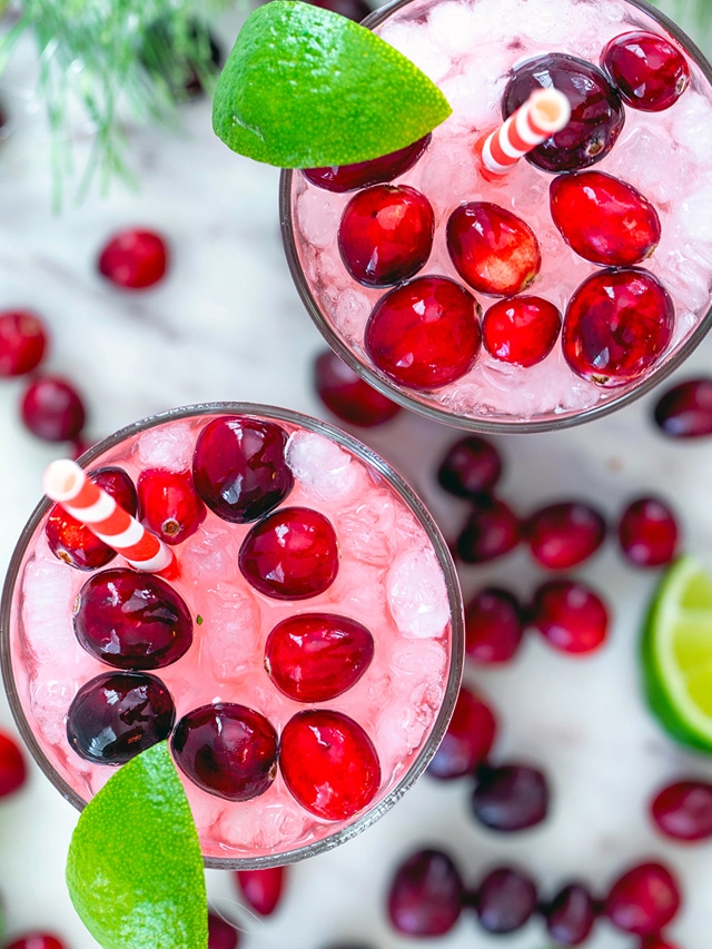 Overhead closeup view of two cranberry mojitos with red and white straws, limes, and cranberries